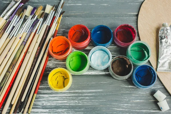 Close up of artist paint brushes, palette and watercolors on grunge gray wooden background. Set of multicolored paints.