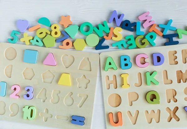 Multicolored wooden toys cubes, pyramid, letters, numbers on white wooden background. Set colorful toys for games in kindergarten, preschool kids. Close up, top view, copy space