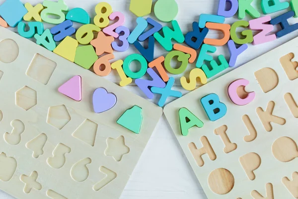 Multicolored wooden toys cubes, pyramid, letters, numbers on white wooden background. Set colorful toys for games in kindergarten, preschool kids. Close up, top view, copy space