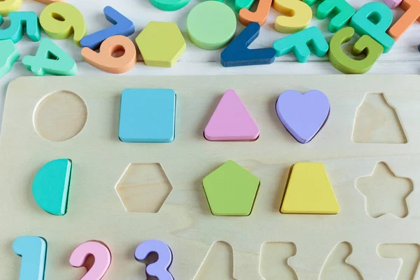 Multicolored wooden toys cubes, pyramid, letters, numbers on white wooden background. Set colorful toys for games in kindergarten, preschool kids. Close up, top view, copy space