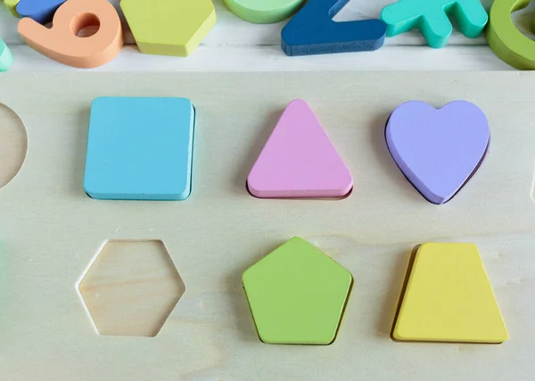 Multicolored wooden toys cubes, pyramid, letters, numbers on white wooden background. Set colorful toys for games in kindergarten, preschool kids. Close up, top view, copy space