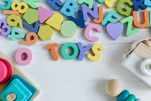 Multicolored wooden toys cubes, pyramid, letters, numbers on white wooden background. Set colorful toys for games in kindergarten, preschool kids. Close up, top view, copy space