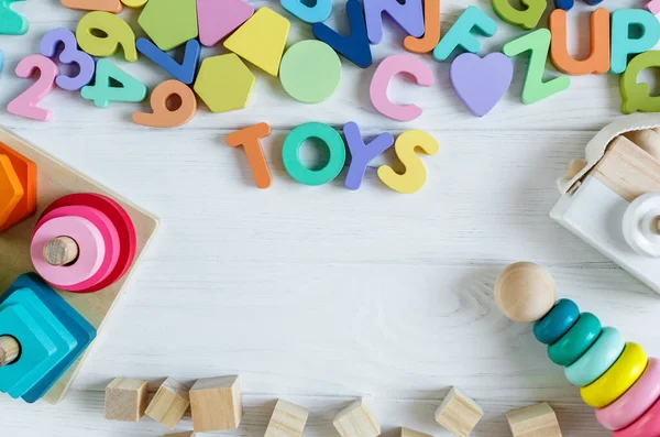 Multicolored wooden toys cubes, pyramid, letters, numbers on white wooden background. Set colorful toys for games in kindergarten, preschool kids. Close up, top view, copy space.