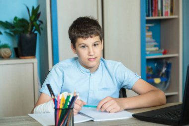 Mavi gömlekli şirin bir çocuk odasında, bilgisayarının yanında oturuyor ve ders çalışıyor. Kulaklık takan genç ev ödevi yapıyor, dinleme dersi alıyor. Ev, uzaklık eğitimi, çocukların kişisel eğitimi..