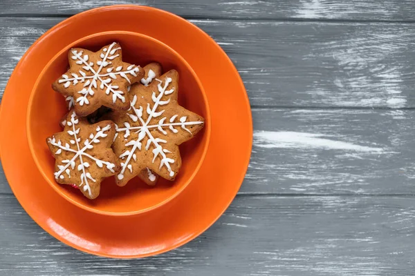 Homemade christmas gingerbread cookies in orange plates on gray wooden background. Snowflake, star, tree, snowman, deer shapes. Holiday, celebration and cooking concept. Close up.