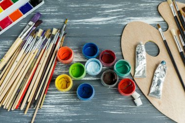 Ressam fırçalarını, paletleri ve suluboyaları grunge gri ahşap arka planda kapatın. Çok renkli boyalar seti. 