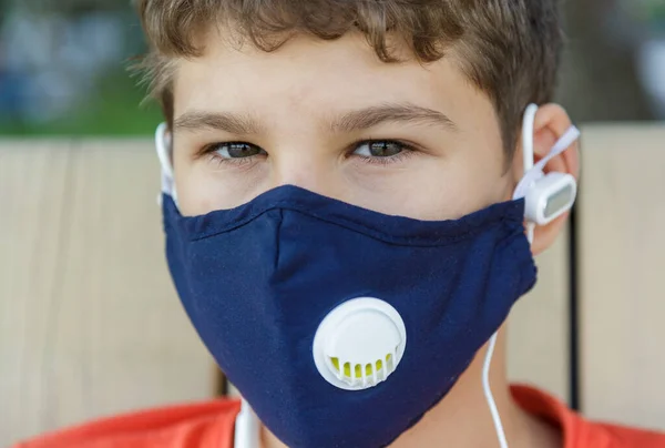 彼の顔に保護マスクでかわいい少年を閉じます コロナウイルス 感染から保護するために医療マスクを身に着けている白いTシャツのティーンエイジャー 街中の隔離 — ストック写真