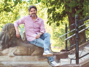 Yetişkin adam zevk oturma bir parkta ağaç yakınındaki gülümseyerek. Doğa, açık oturan toplam veya tam uzunluğu kişi