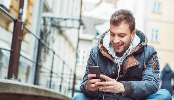 Jovem Feliz Segurando Seu Smartphone Enquanto Mensagens Texto Algo Sentado — Fotografia de Stock