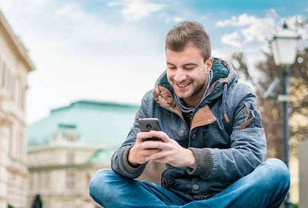 Jovem Satisfeito Segurando Seu Telefone Enquanto Mensagens Texto Algo Sentado — Fotografia de Stock