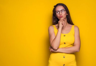Skeptical woman thinking. Ask. Thoughtfully girl with confusion face expression, isolated on yellow background. Copy space. Decided female person. Studio shot