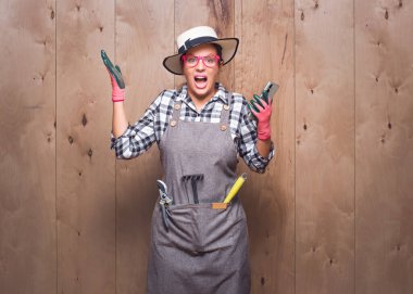 Trendy gardener woman with phone unexpected incredible notification on wooden background in studio. Amazed female farmer using smart phone. Studio shot