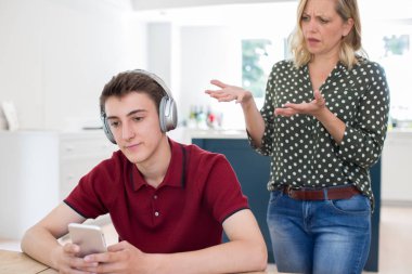 Kulaklıklar giyen ve cep telefonuyla annesi tarafından evde Nagged genç çocuk