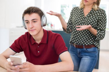 Kulaklıklar giyen ve cep telefonuyla annesi tarafından evde Nagged genç çocuk