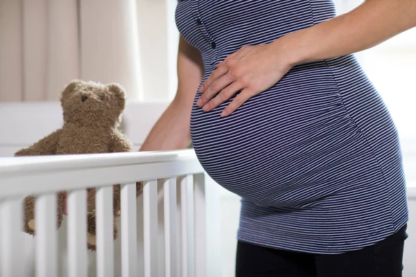 关闭怀孕妇女把泰迪熊到婴儿床在托儿所 — 图库照片
