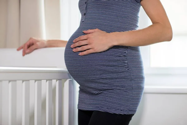 关闭的孕妇接触胃站在婴儿床旁边的托儿所 — 图库照片