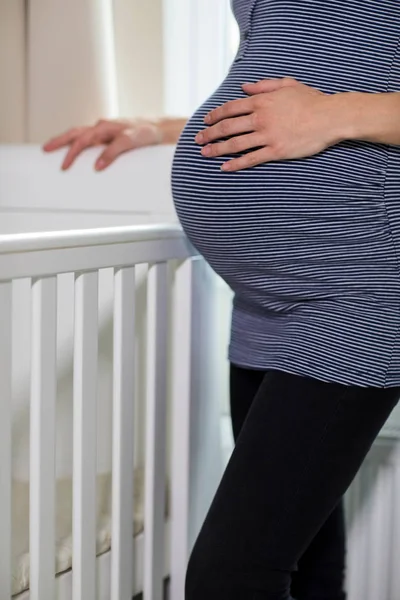 关闭的孕妇接触胃站在婴儿床旁边的托儿所 — 图库照片