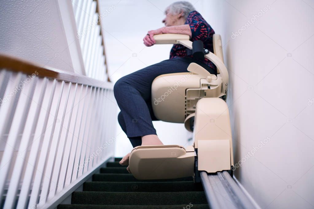 Senior Woman Sitting On Stair Lift At Home To Help Mobility