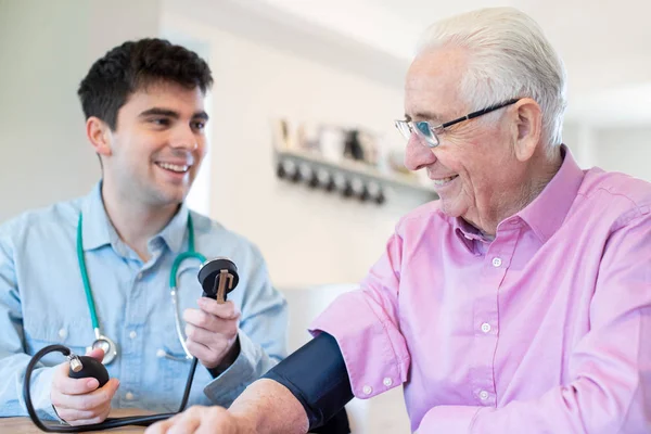 Lekarz mężczyzna pomiaru ciśnienia krwi z starszy mężczyzna w domu — Zdjęcie stockowe
