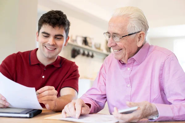 Junger Mann hilft Seniorin bei Papierkram zu Hause — Stockfoto