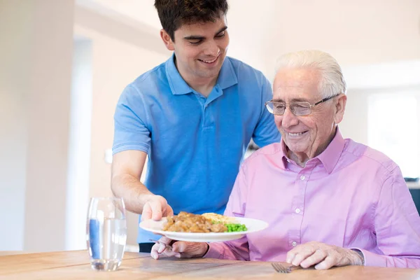 Male Care Assistant Serving Meal To Senior Male Seated At Table — Stock Photo, Image