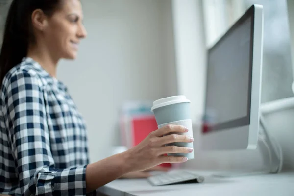 Mujer trabajando en la computadora bebiendo de la taza reutilizable para llevar — Foto de Stock