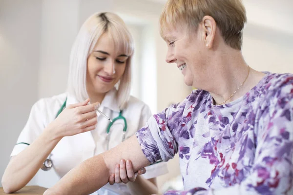 Жінка медсестра дає старшій жінці ін'єкції в руку з шприцом — стокове фото