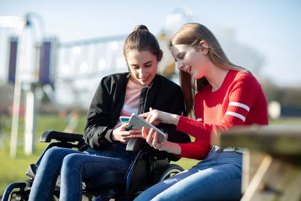 Teenager im Rollstuhl schaut mit Freundin auf Handy — Stockfoto