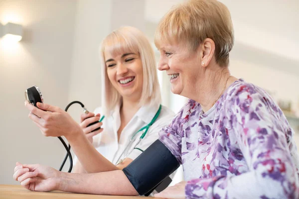 Meten van de bloeddruk van Senior vrouw thuis verplegen — Stockfoto