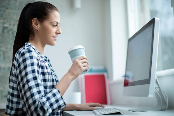 Mujer trabajando en la computadora bebiendo de la taza reutilizable para llevar — Foto de Stock