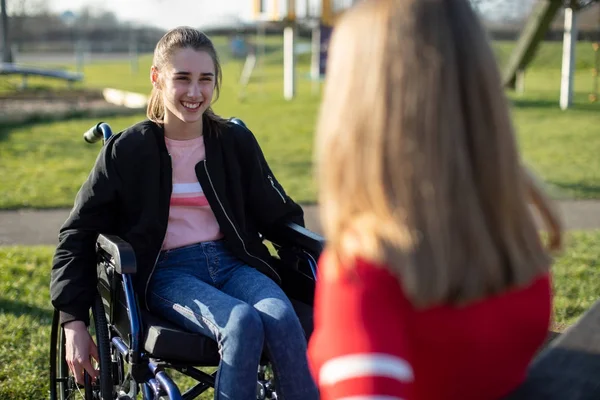 Adolescente chica en silla de ruedas hablando con un amigo en el parque —  Fotos de Stock