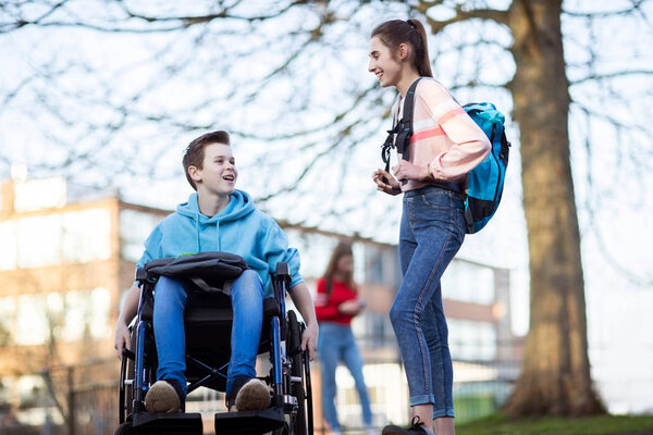 Teenage Boy In Wheelchair Talking with Female Friend As They Lea
