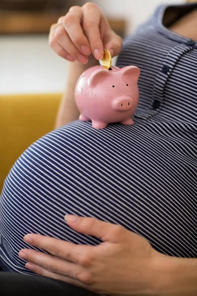 Primer plano de la mujer embarazada poniendo monedas en Piggybank equilibrado — Foto de Stock