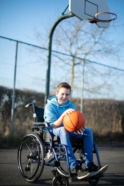Porträt eines Teenager-Jungen im Rollstuhl beim Basketballspielen auf outd — Stockfoto