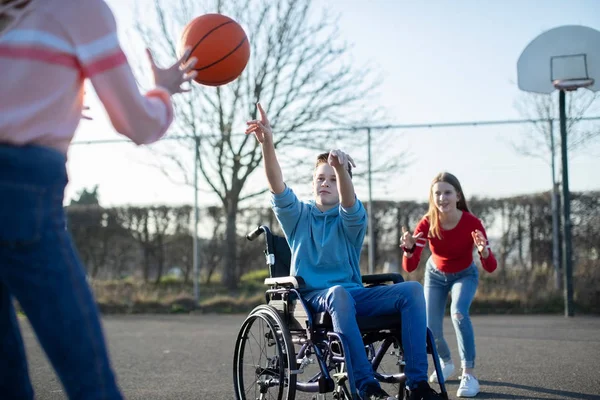 Arkadaş grubu basketbol oynarken tekerlekli sandalyede genç çocuk — Stok fotoğraf