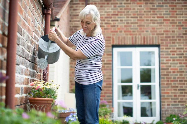 Senior nő öntözés növények öntözési lehet a Garden otthon — Stock Fotó