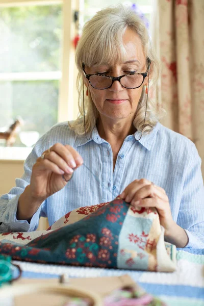 Старша жінка вишиває кришку подушки вдома — стокове фото
