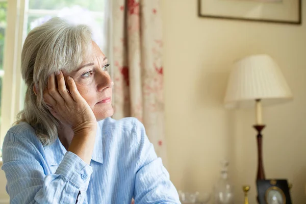 Senior kvinna som lider med depression tittar ut genom fönstret på — Stockfoto
