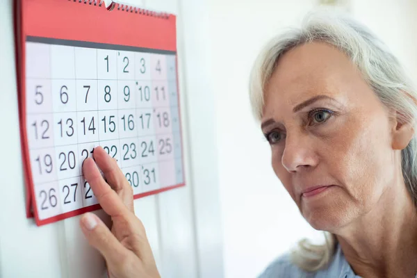 Збентежена старша жінка з деменцією дивиться на настінний календар — стокове фото