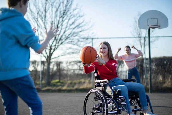 Девушка-подросток в инвалидной коляске играет в баскетбол с друзьями — стоковое фото