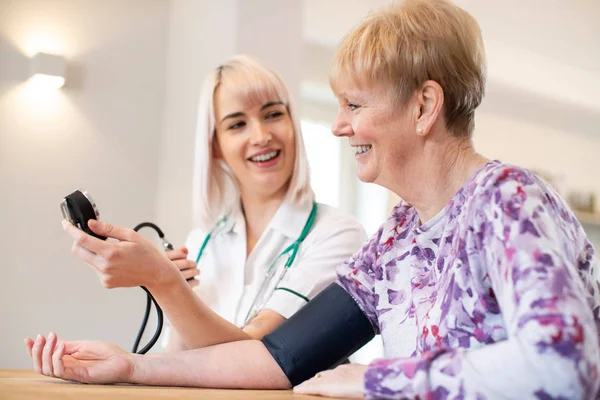 Enfermera que mide la presión arterial de una mujer mayor en casa —  Fotos de Stock