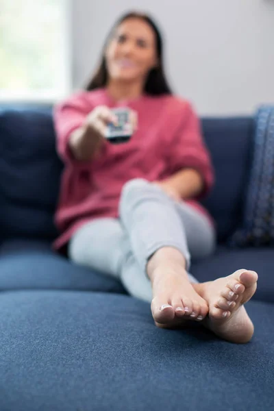 Mujer relajándose en sofá sosteniendo control remoto y viendo telev — Foto de Stock