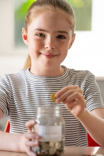 Retrato de niña poniendo monedas en tarro de vidrio etiquetado ahorros A — Foto de Stock