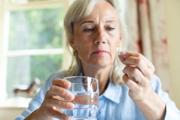 Femme âgée prenant tablette avec verre d'eau à la maison — Photo
