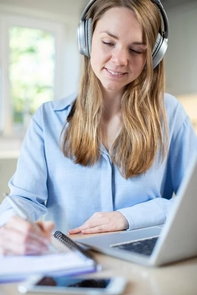 Mujer estudiando en casa usando el ordenador portátil y el uso de auriculares — Foto de Stock