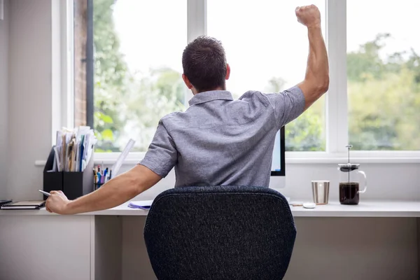 Rear View Of Man Working From Home On Computer  In Home Office Stretching At Desk