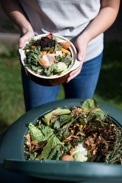 Close Up Of Woman Emptying Food Waste Into Garden Composter At Home