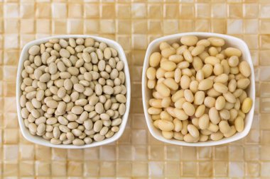 Batırılmış ve fasulye bezelye, Donanma fasulye, kurutulmuş Pearl kuru, Boston bean üstten görünüm (Phaseolus vulgaris sarı seramik zemin üzerine beyaz kase)