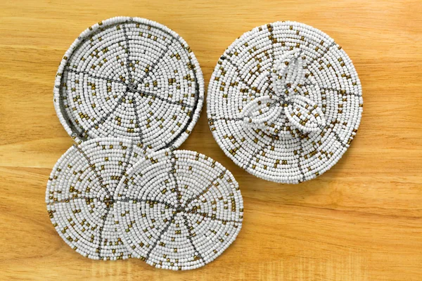 Round African handmade Beaded Coaster set in white gold on wooden background