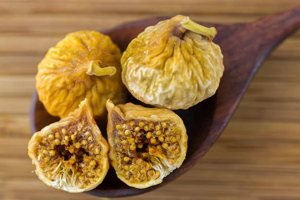 Dried fig fruit cut in half showing seeds on dark wooden spoon on wood background — Stock Photo, Image